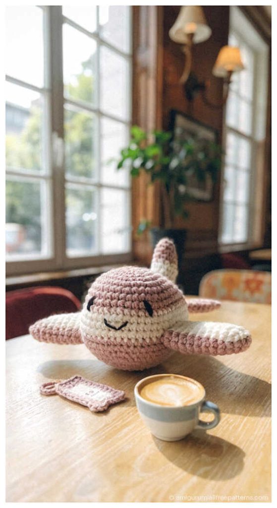 Soft pink airplane amigurumi placed on cafe table with coffee cup, styled as a handmade crochet decor piece for cozy nursery or kids room theme.