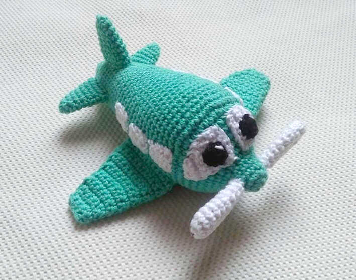 Green amigurumi airplane crochet toy with white propeller and big eyes, designed as a cute handmade kids gift, free crochet pattern available online.
