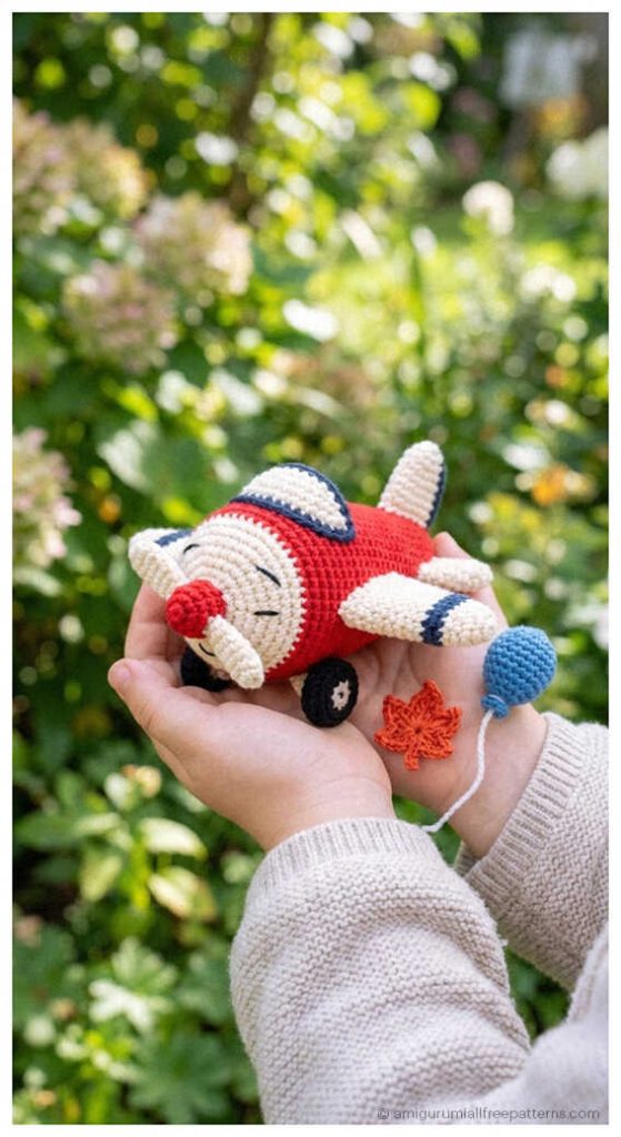 Red and white airplane amigurumi held outdoors, styled as a handmade crochet baby gift for boys nursery or travel themed kids room.