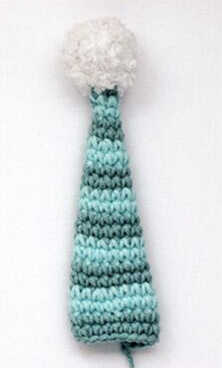 Crochet amigurumi hat with pom pom made for the Bjashik doll, long striped cap crocheted in blue tones with fluffy white pom detail.