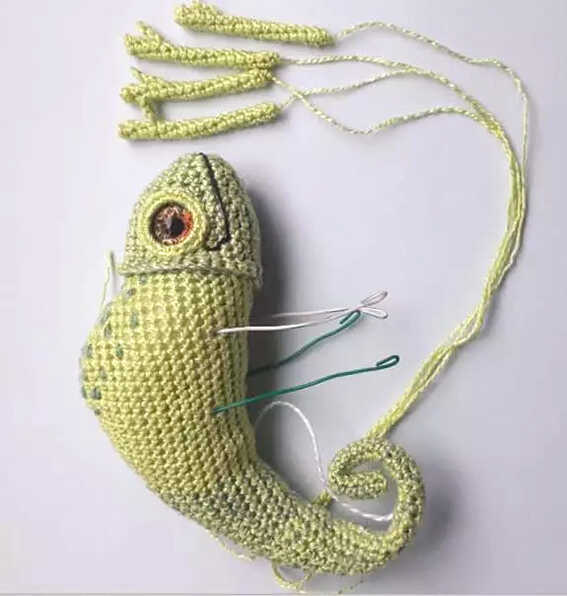 Chameleon amigurumi crochet assembly showing body and separate legs pieces before attachment, detailed handmade lizard toy process for crochet pattern.