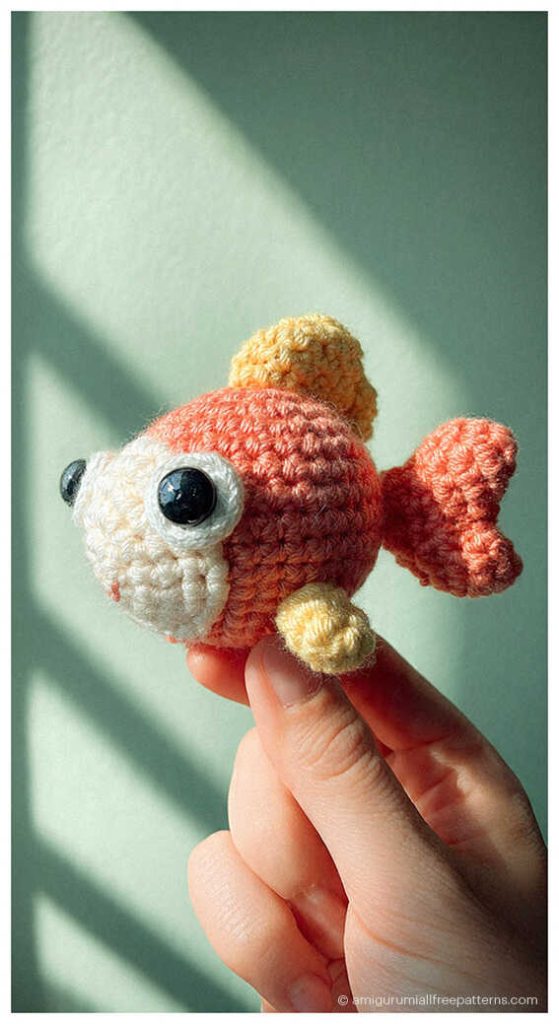 Fish amigurumi crochet doll in blue yarn held between fingers, tiny handmade plush you’ll want to make for gifts or nursery decor.