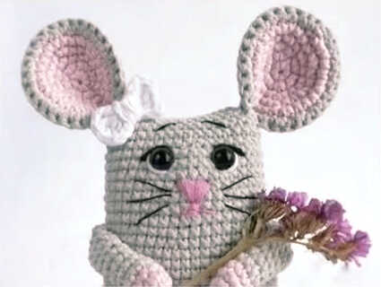 Cute little mouse amigurumi crochet doll holding tiny flowers, handmade plush toy design with pink ears, free crochet pattern for a sweet handmade gift idea.