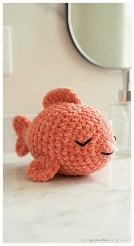 Fish amigurumi crochet toy in soft coral yarn on table, cute handmade plush you’ll want to make for nursery decor or gift idea.