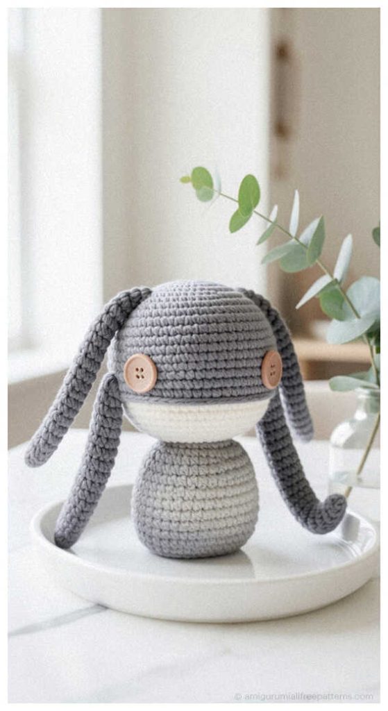 Cute gray alien amigurumi crochet doll with long ears displayed on tray, styled as a handmade sci fi plush toy for desk decor or gift idea.
