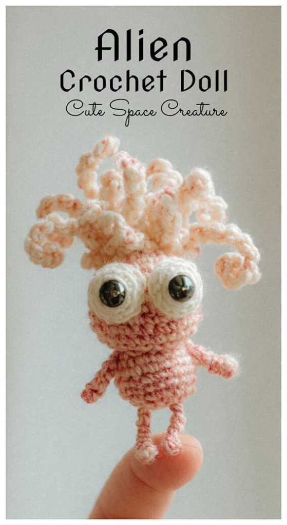 Mini alien crochet doll with curly antenna hair held on fingertip, styled as a cute handmade space creature plush for desk decor or collectible gift.