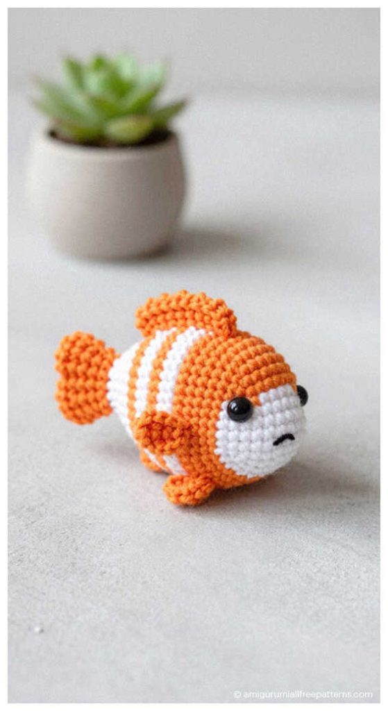 Fish amigurumi crochet doll in clownfish colors on table, cute handmade plush perfect for nursery decor or a sweet crochet gift idea.