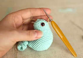 Bird amigurumi crochet beak detail being stitched on body, small crochet piece shown in hand during assembly step for a simple amigurumi pattern.