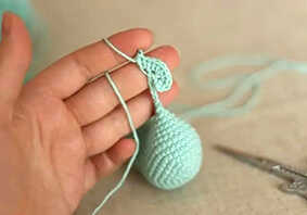 Bird amigurumi crochet tail piece being attached to body, small crochet detail shown in hand during assembly step for a simple amigurumi pattern.