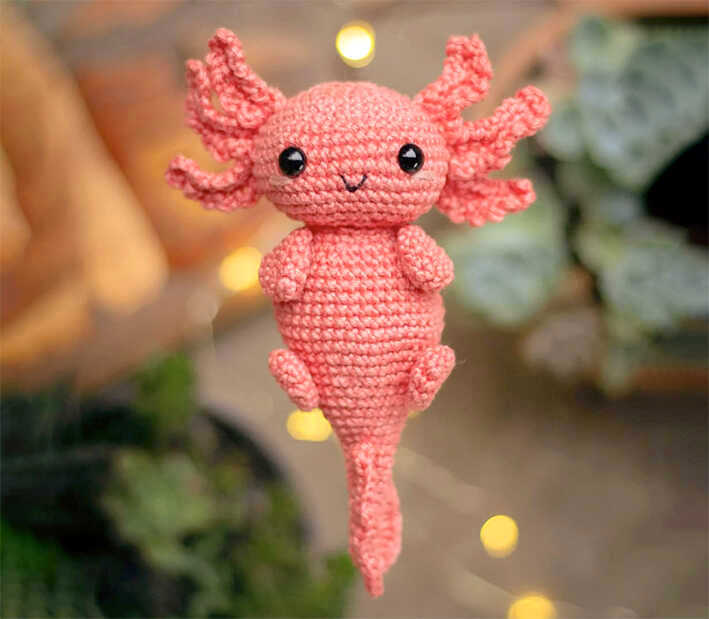 Pink axolotl amigurumi crochet plush displayed in warm soft lighting