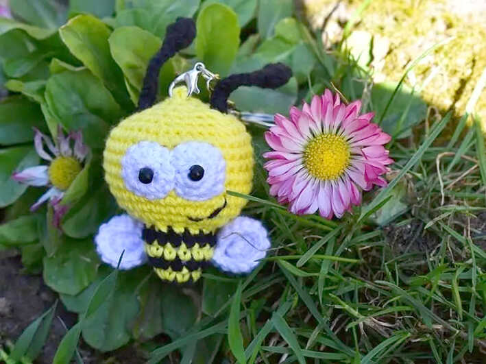 Bee crochet keychain amigurumi displayed outdoors beside flowers