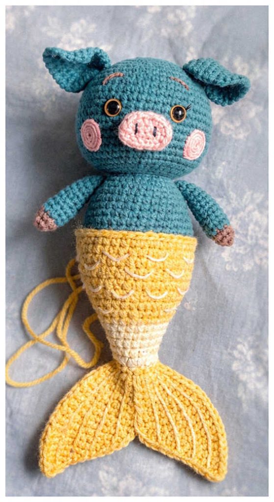 Blue pig mermaid crochet plush displayed in a cozy styled setting