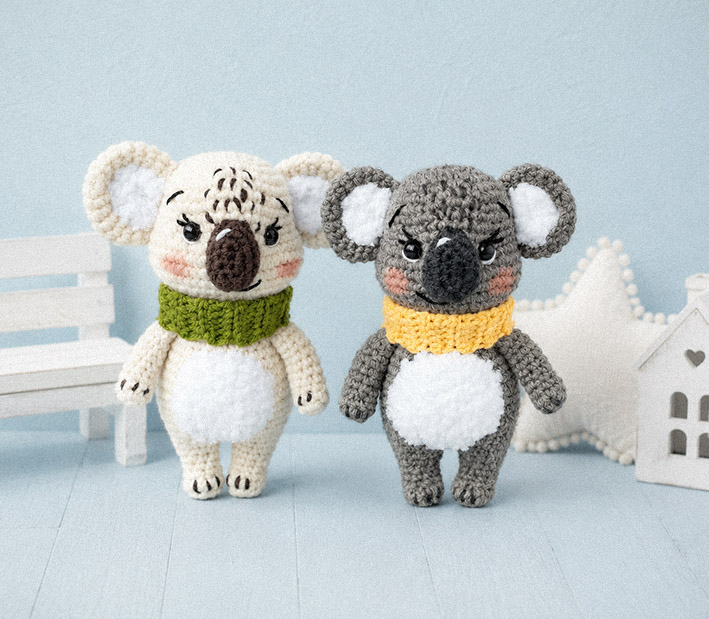 Two koala amigurumi crochet plush toys displayed in a soft styled indoor scene