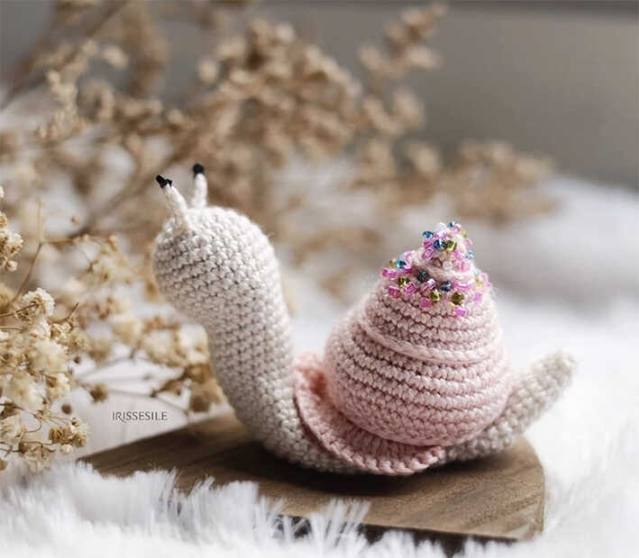 Crochet snail amigurumi plush displayed in a soft cozy styled setting