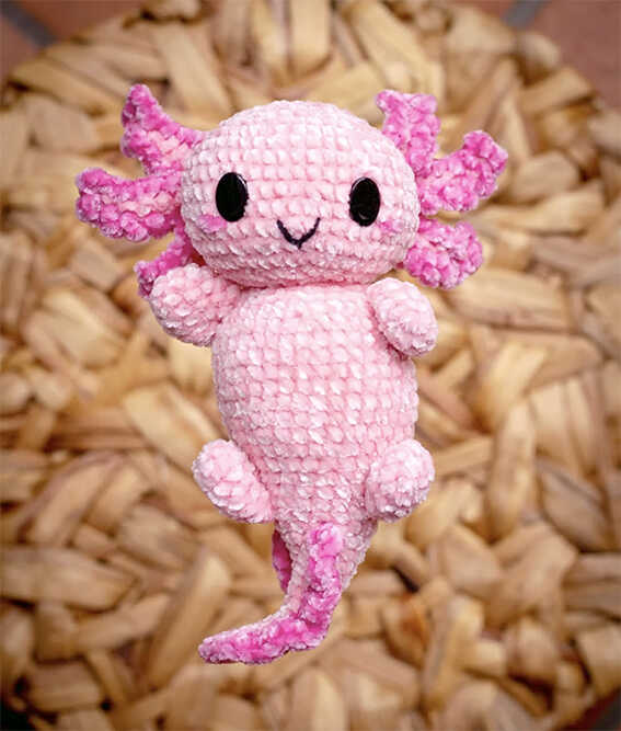 Cute pink axolotl amigurumi plush displayed on a textured background