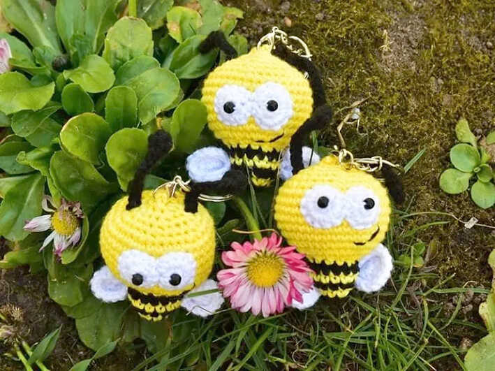 Cute bee crochet keychain amigurumi collection displayed outdoors with flowers