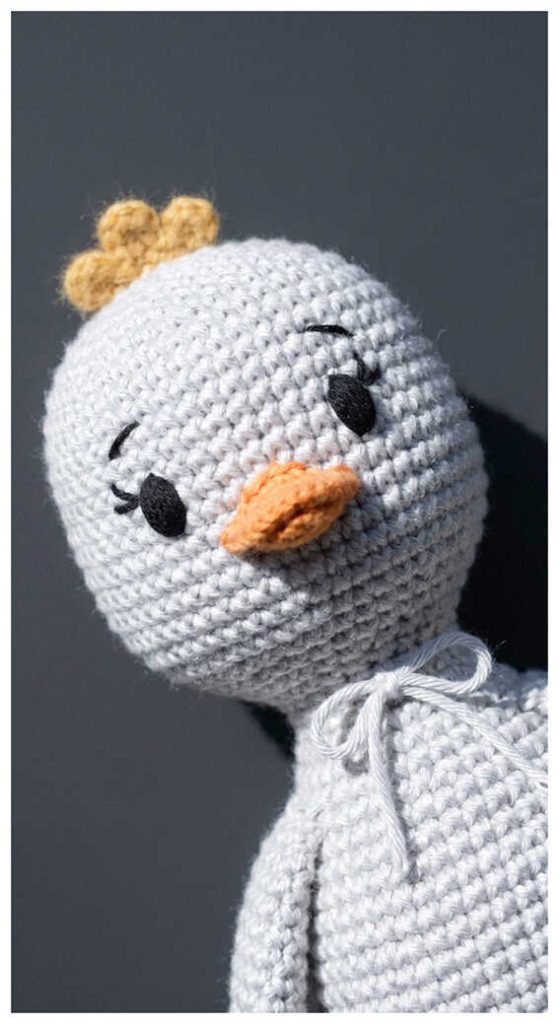 Gray duck crochet plush wearing a scarf on a dark background