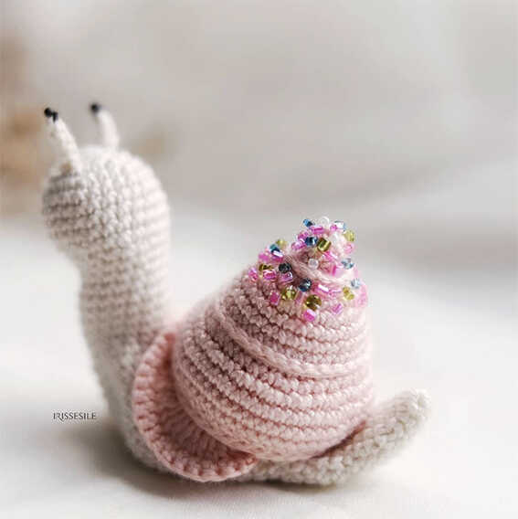 Pink crochet snail amigurumi displayed in a soft cozy indoor setting