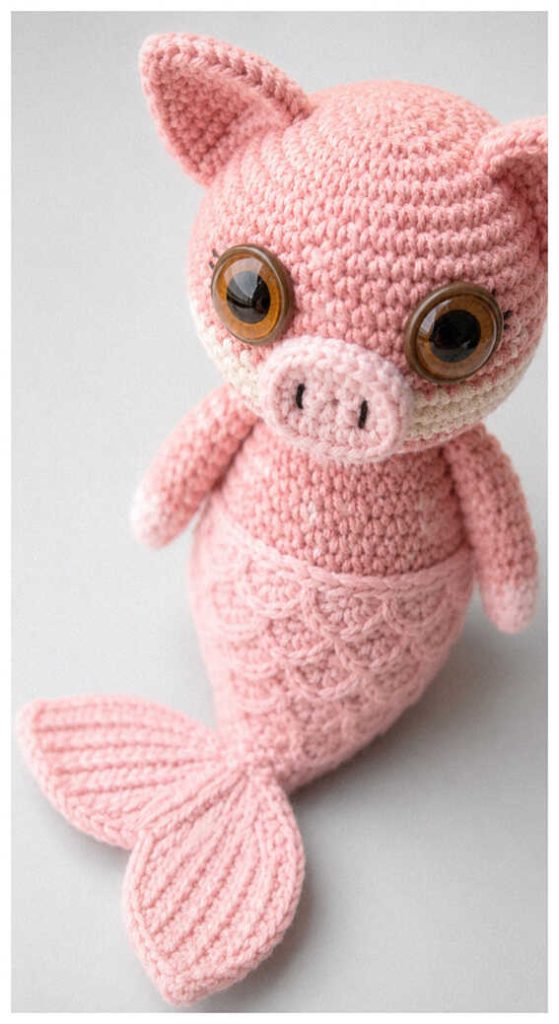 Pink pig mermaid amigurumi plush displayed in soft indoor lighting