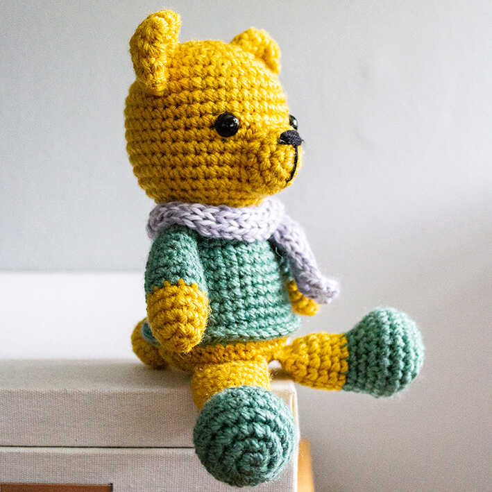 Small crochet bear amigurumi plush side view with scarf displayed indoors