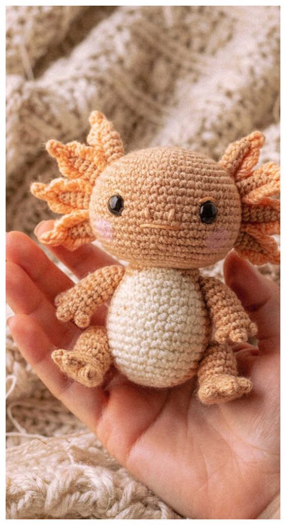 Tiny axolotl amigurumi plush held in hand in a cozy setting