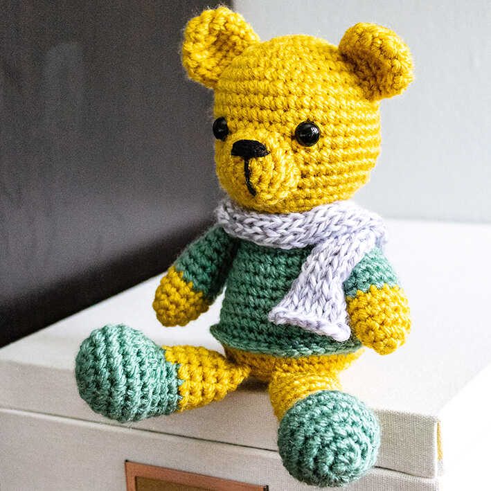 Tiny crochet bear amigurumi plush with scarf displayed on a table