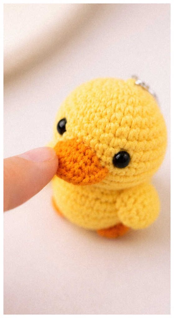 Tiny duck crochet plush held between fingers in a bright setting