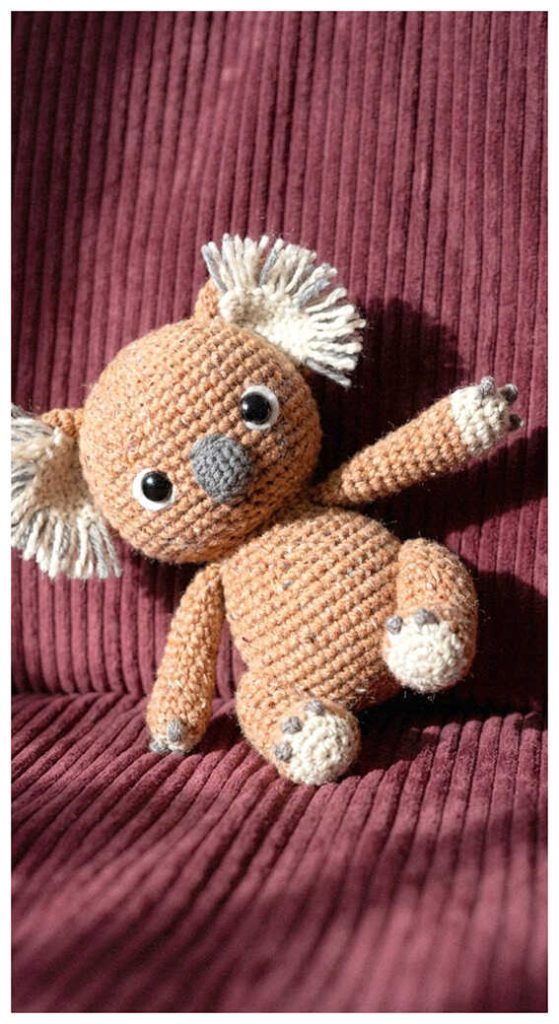 Tiny koala crochet plush resting on textured fabric