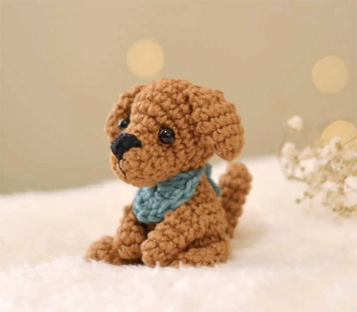 Tiny crochet puppy amigurumi with bandana displayed in soft warm lighting